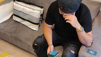 Nuori istuu sohvalla kännykkä kädessä.