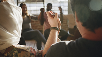 Ryhmä ihmisiä istuu piirissä kädet yhdessä